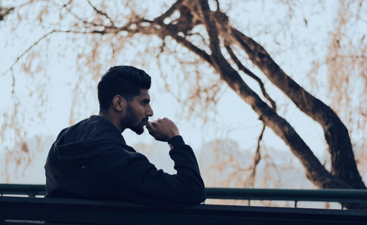 Man in deep thought sitting on a bench in a serene autumn park setting.