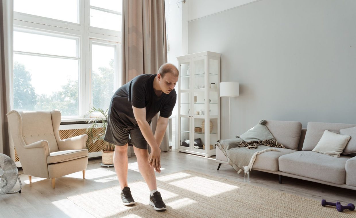 Man performing a stretching exercise in a sunlit living room, embracing a healthy lifestyle.