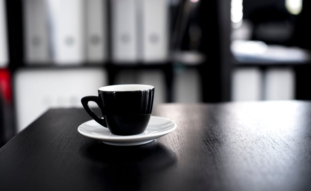 Black coffee cup on a wooden desk in an office setting. Minimalist and modern interior design vibe.
