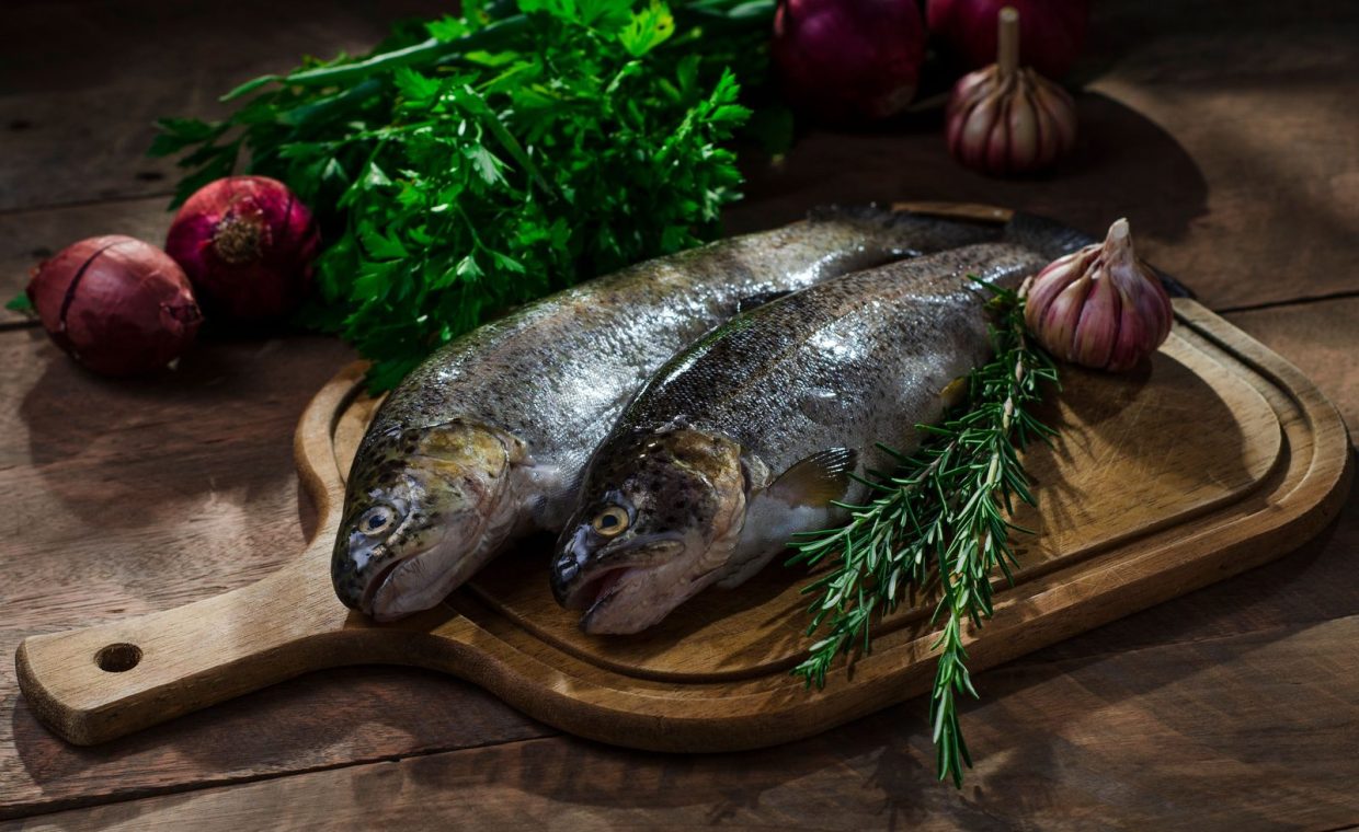 Fresh whole fish on a wooden board with herbs and vegetables, perfect for culinary presentations.