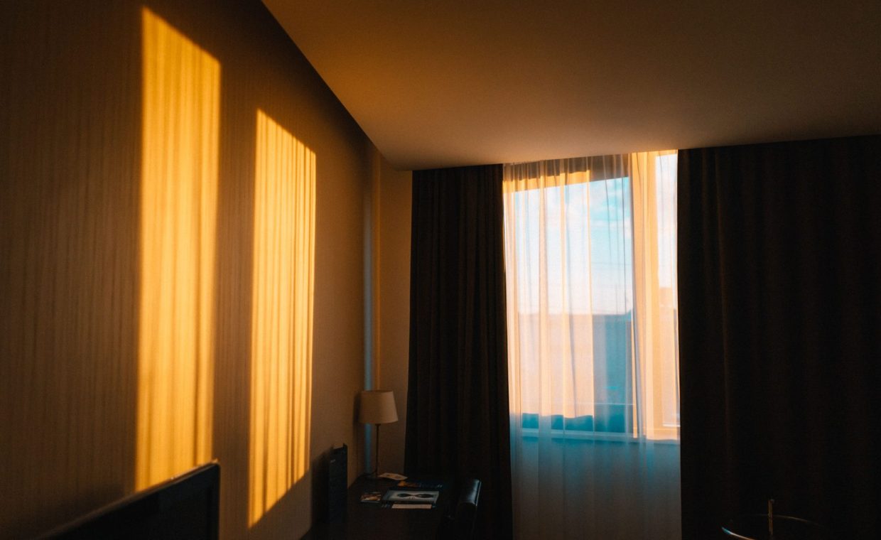 A contemporary hotel room draped in warm morning light casting shadows on the wall.