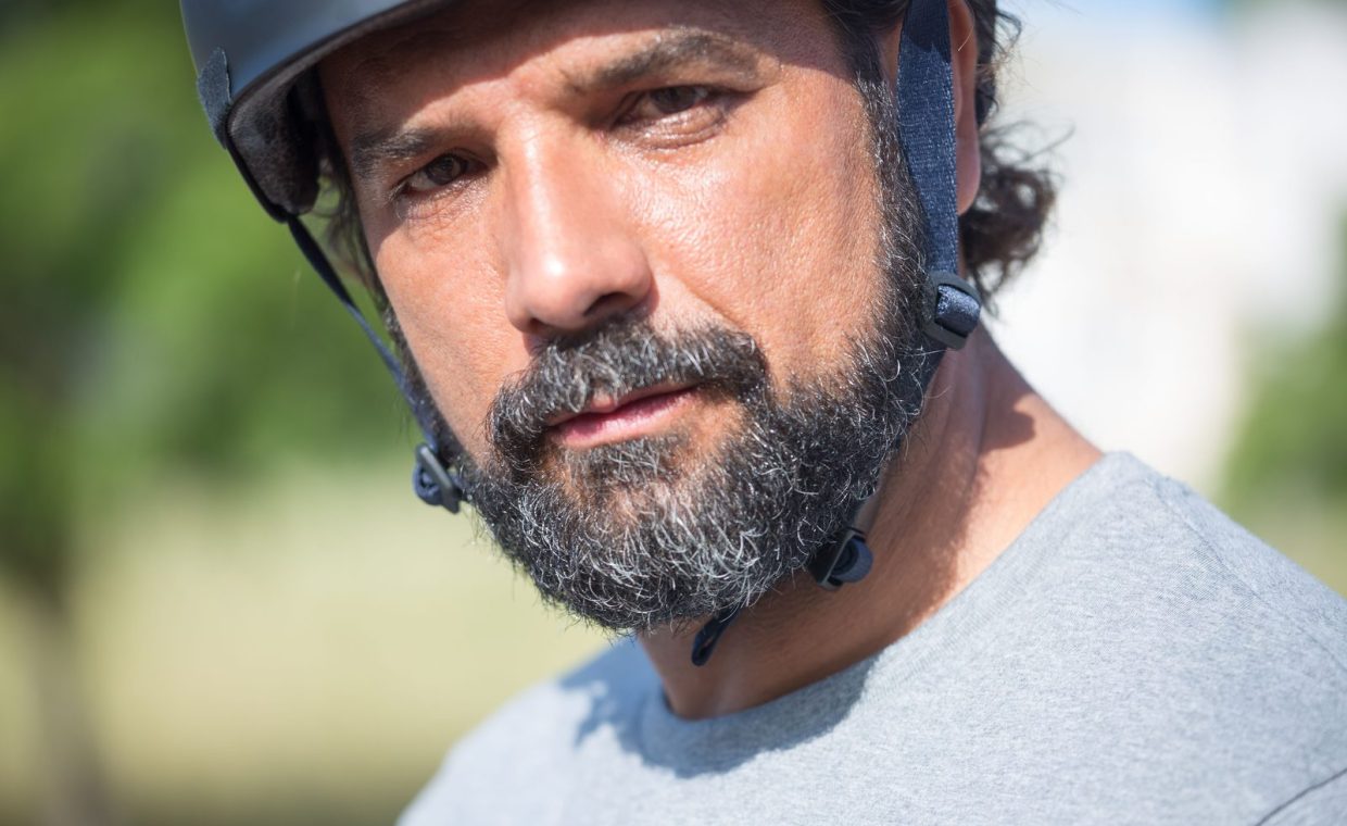 An engaging close-up portrait of a bearded man wearing a helmet, captured outdoors in daylight.