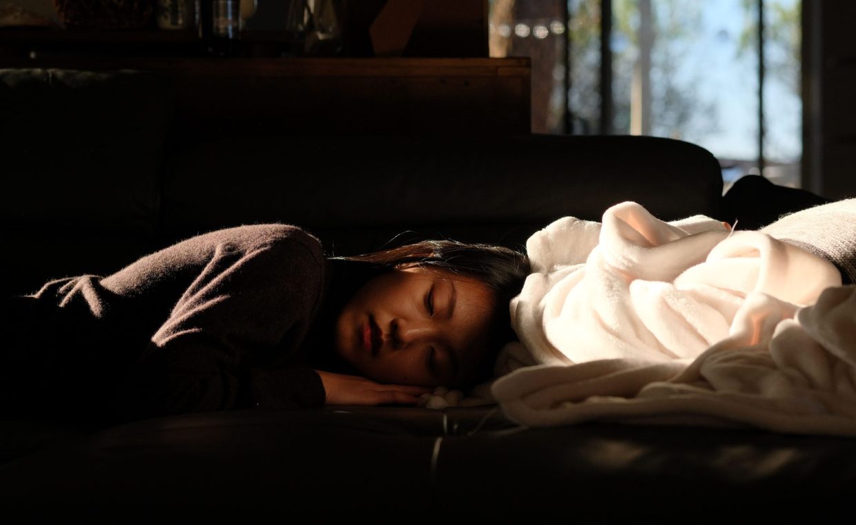 A woman peacefully sleeping on a couch with sunlight streaming in through the window.
