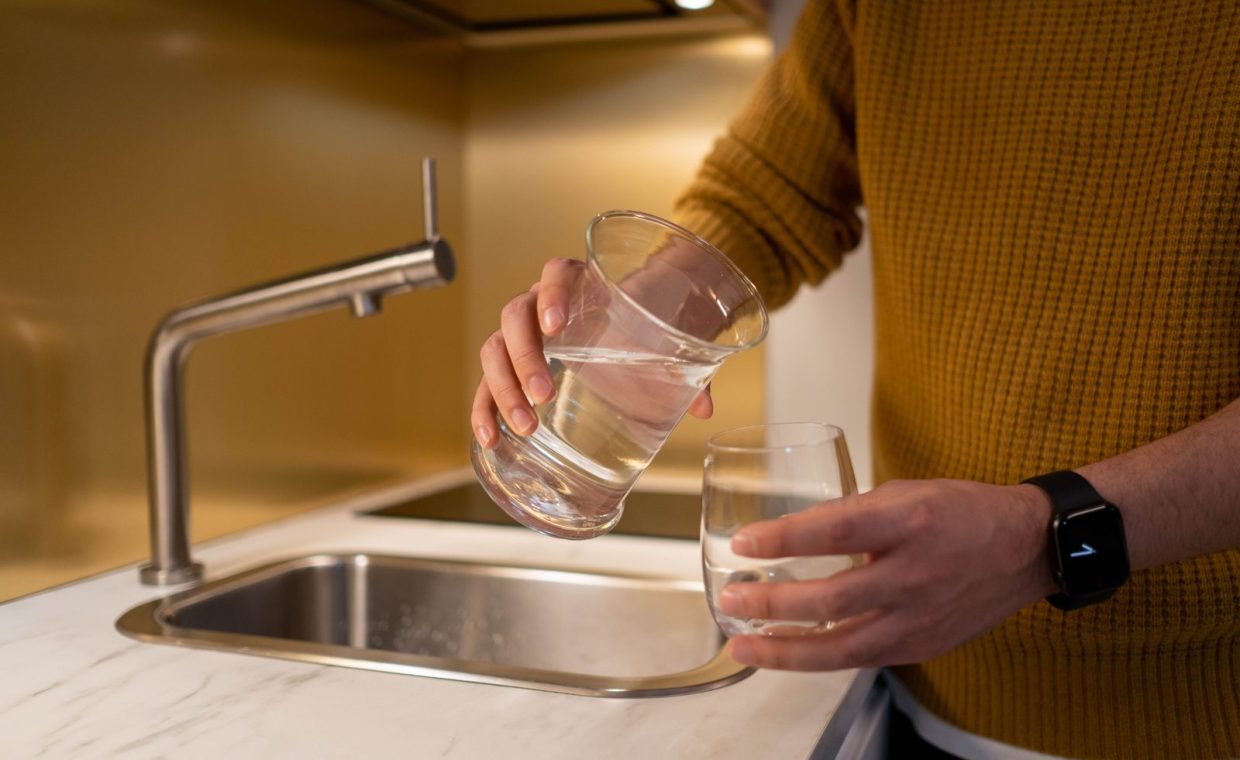 Person pouring water from a pitcher into a glass in a contemporary kitchen setting.