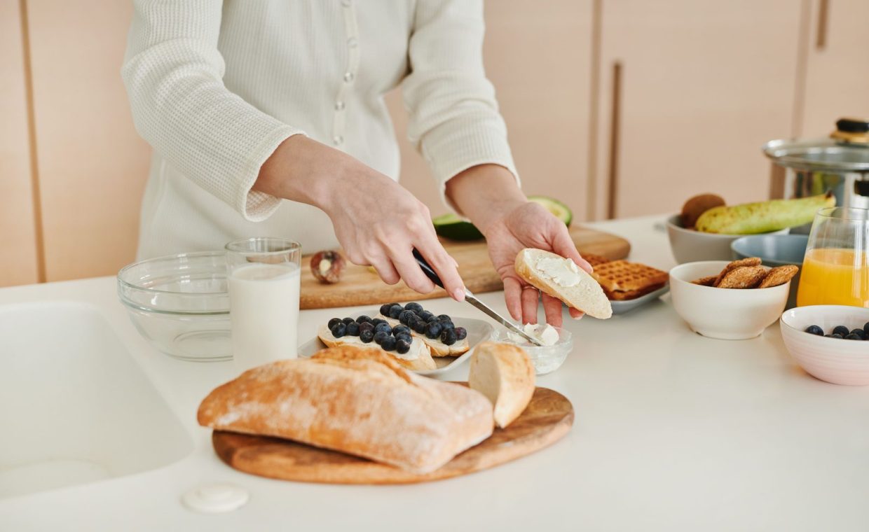 Woman spreads cream on bread with blueberries. A wholesome breakfast setup.