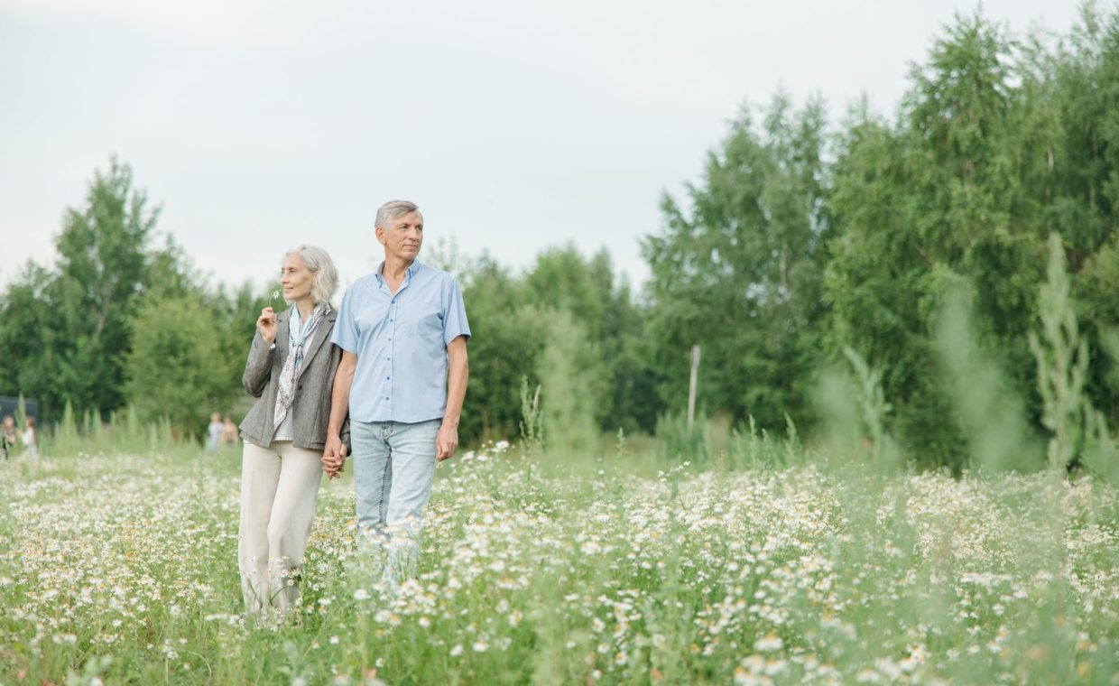 A senior couple enjoying a peaceful walk through a lush flower field on a sunny day.