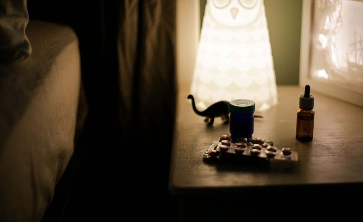 Dimly lit bedside table featuring an owl lamp, medicine bottles, and pill packets, creating a cozy night ambiance.