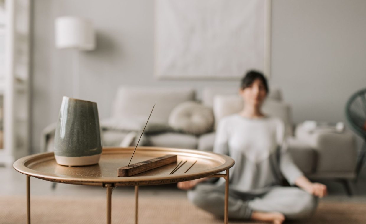 Calm living room scene with incense and a woman meditating, perfect for relaxation concepts.