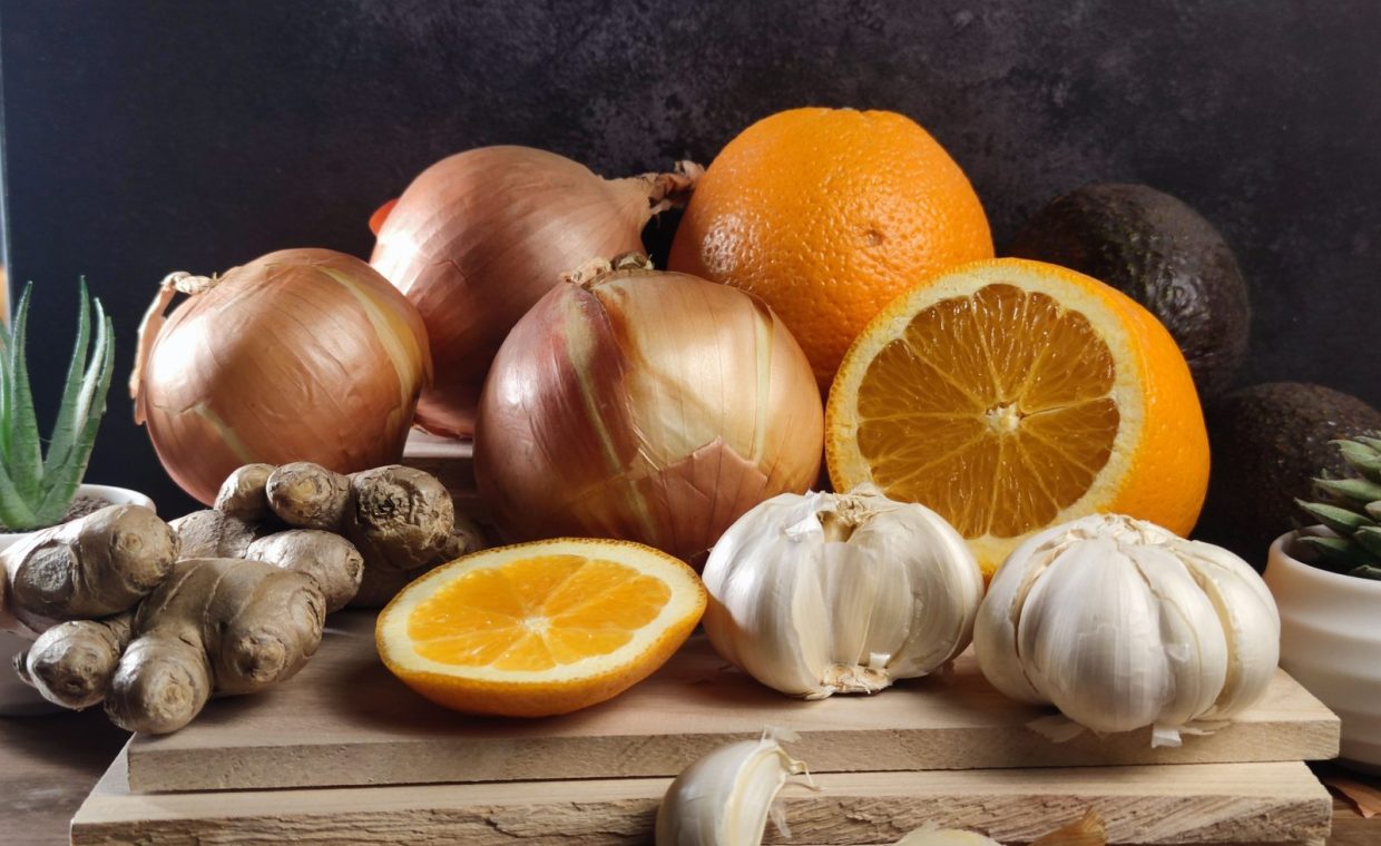 Fresh oranges, onions, garlic, and ginger arranged on a wooden board, perfect for healthy lifestyle visuals.