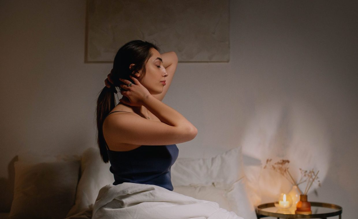 A calm woman sits on a bed in a cozy bedroom, enjoying a peaceful moment.